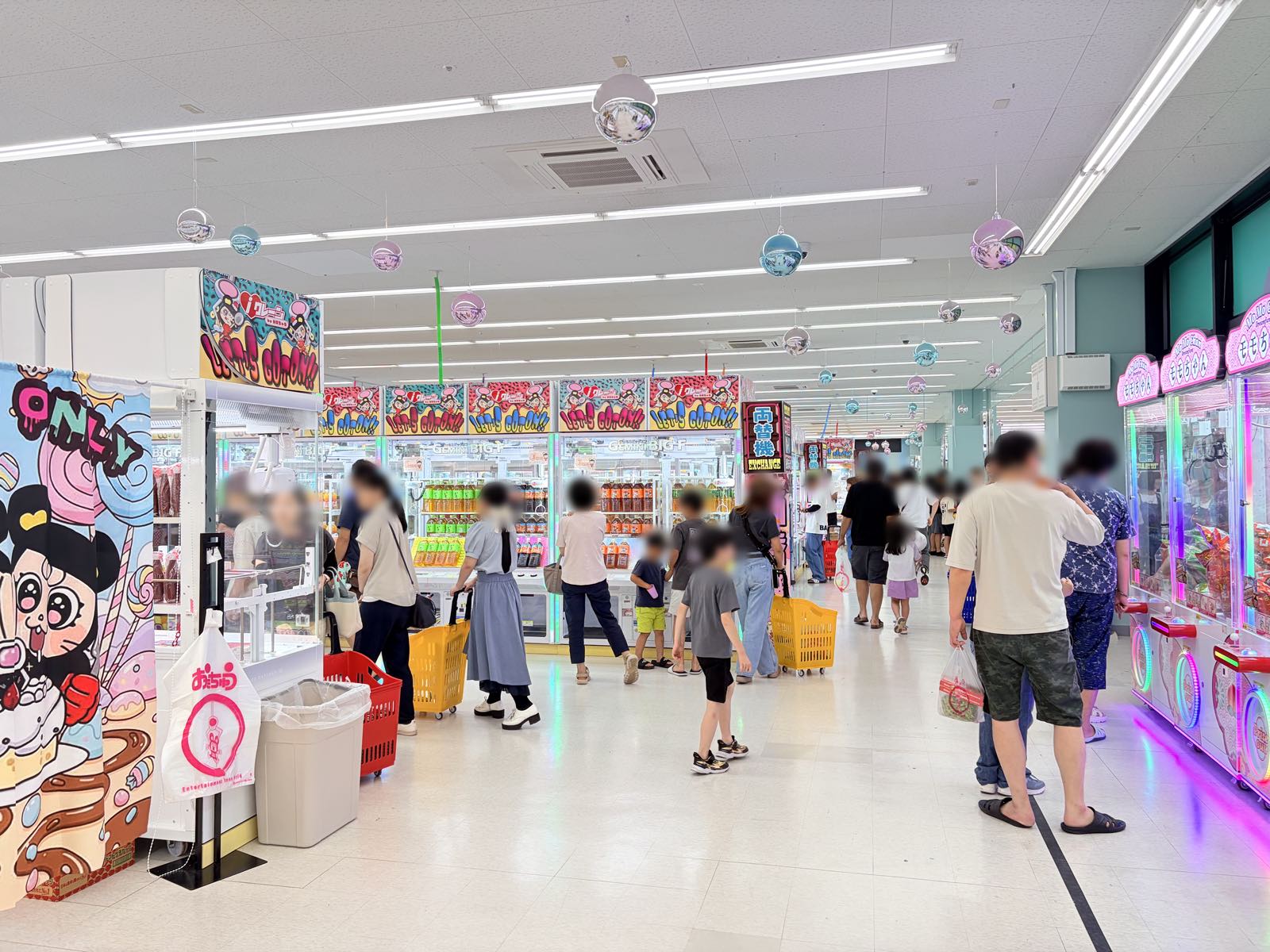 iクレーン三条店の店内奥。ペットボトル飲料がぎっしり詰まったクレーンゲーム台がずらりと並び、買い物カゴを持った来店客が行き交っている