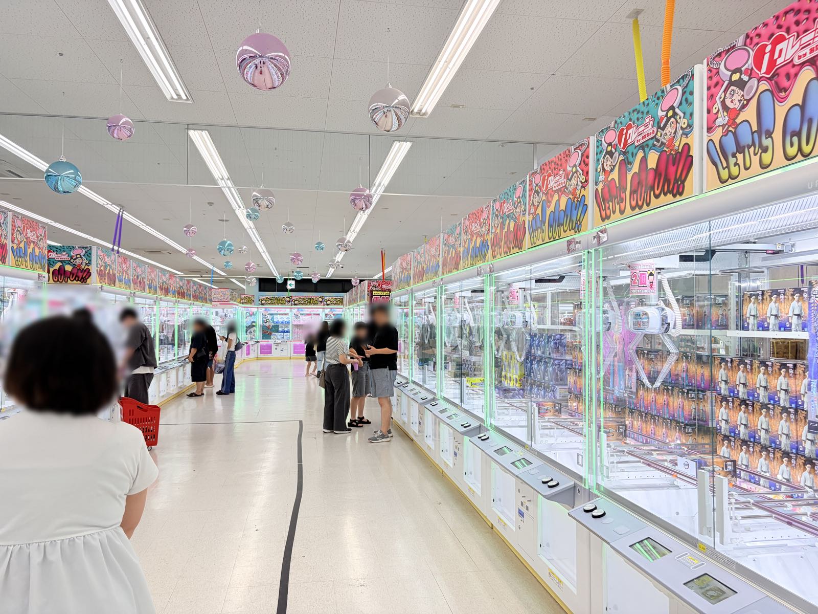 フィギュアが並ぶクレーンゲーム台が通路の右側にずらりと続くフロア。台の上部には「LET'S GO!!」とiクレーンのロゴが入ったカラフルなPOPが掲げられている