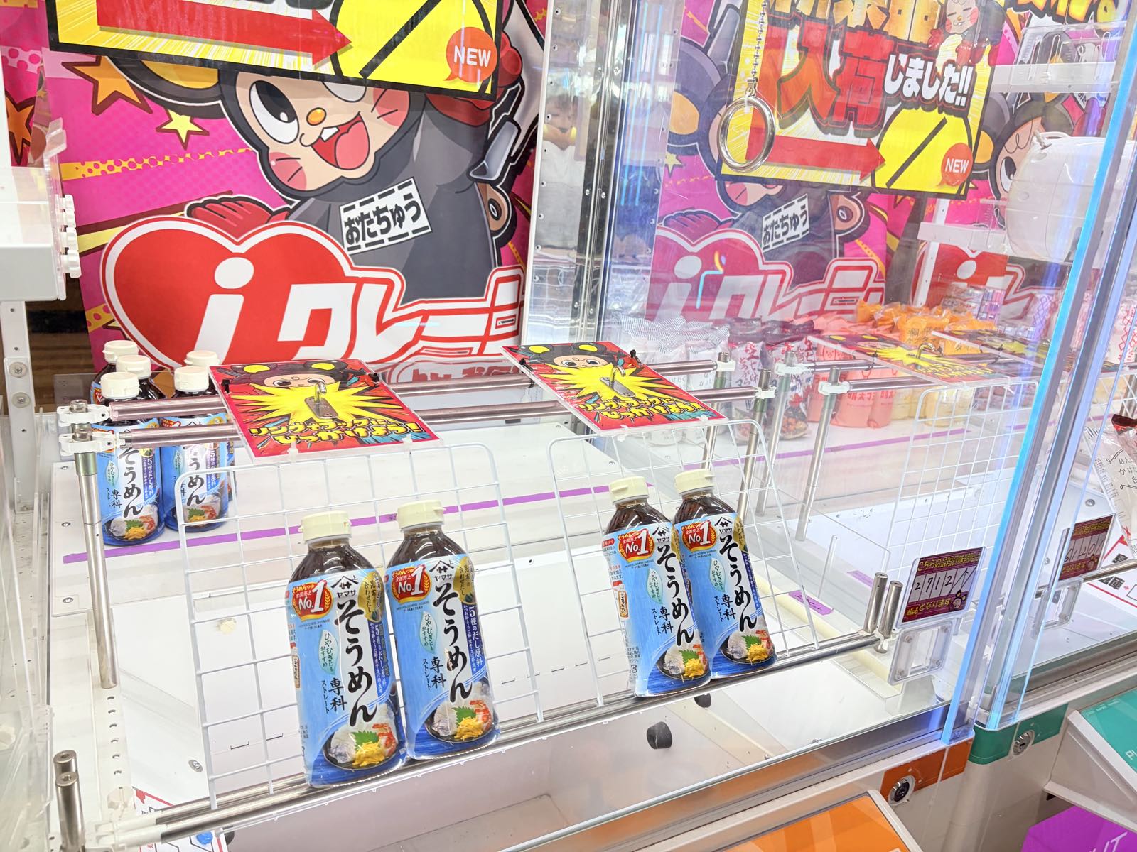 そうめん専科のボトルが白いワイヤーラックに並んだフック設定台。奥にはiクレーンのロゴと「入荷しました!!」のPOPが掲示され、右上にはチェーンから下がったリングが見える