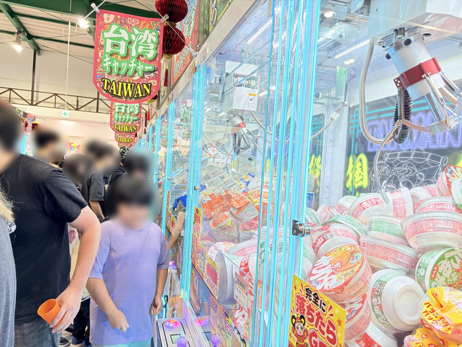 遊とぴあ新潟店の台湾キャッチャー。カップ麺や袋麺、お菓子が台にぎっしり積まれ、「完全に落ちたらGET」の掲示が貼られている