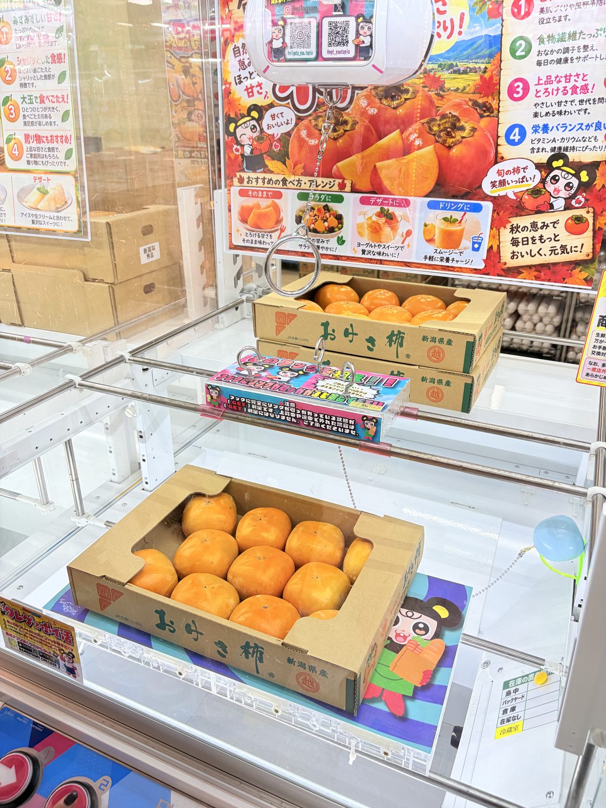 遊とぴあ新潟店のフック設定の台。新潟県産のおけさ柿の箱が景品で、リングの付いたチェーンが下がり、フックにリングが引っかかった状態がGETになるという注意書きが付いている