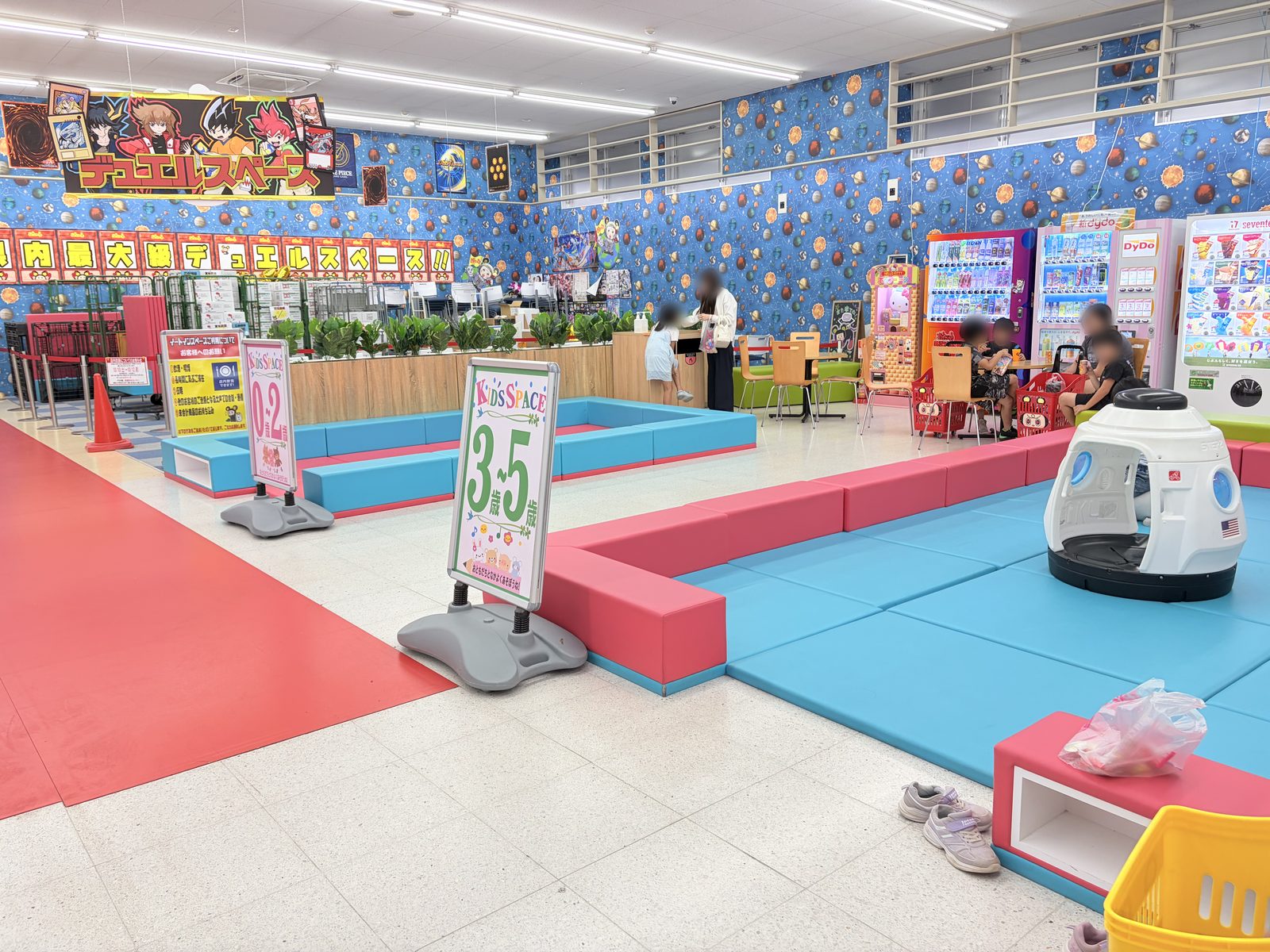 おたちゅう新潟本店のキッズスペース。マットで囲まれた区画に「0〜2歳」「3〜5歳」のサインが立ち、奥にデュエルスペースの掲示がある